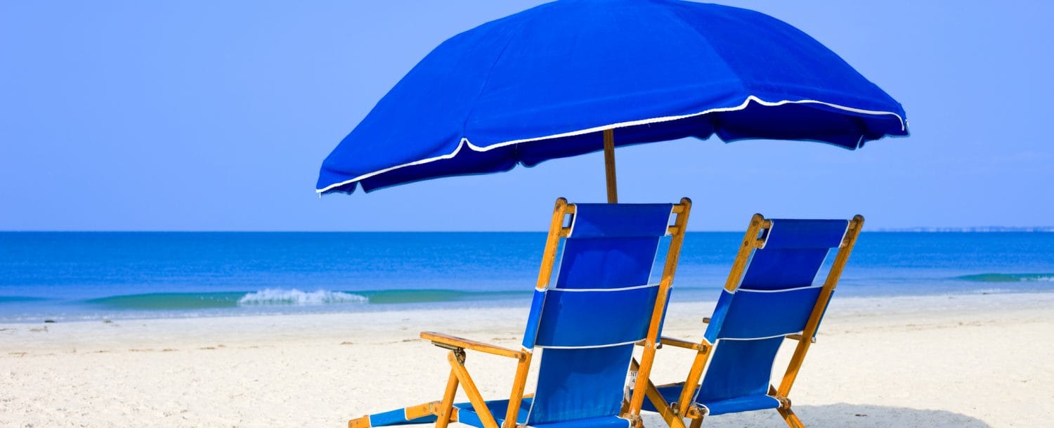 White sandy beach with two blue beach loungers and umbrella