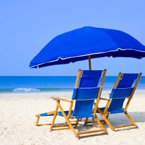 White sandy beach with two blue beach loungers and umbrella