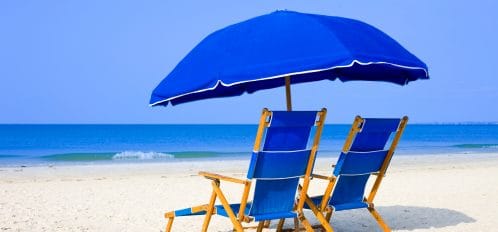 White sandy beach with two blue beach loungers and umbrella