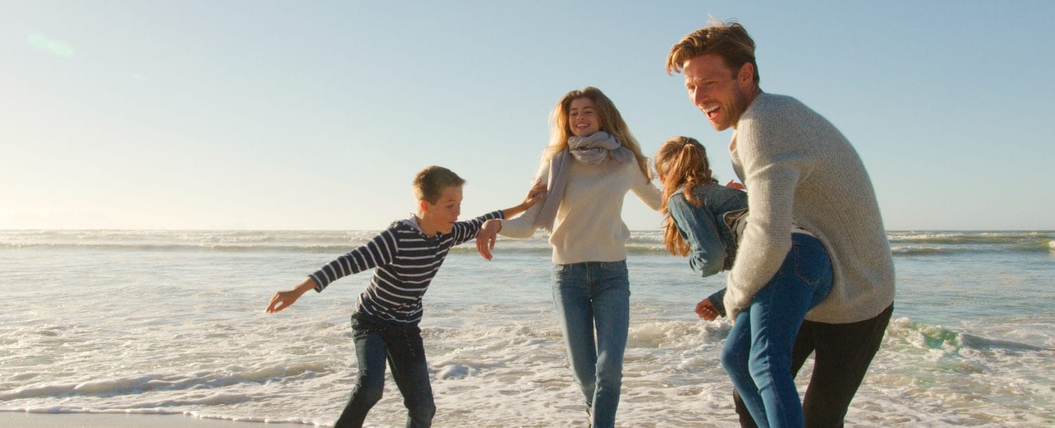 Family On Winter Beach Running Away From Advancing Waves