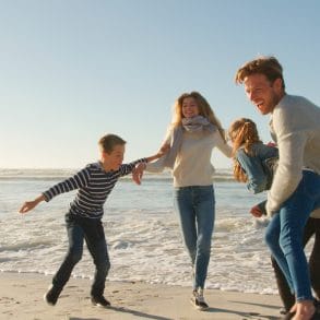 Family On Winter Beach Running Away From Advancing Waves