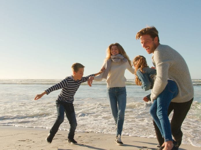 Family On Winter Beach Running Away From Advancing Waves