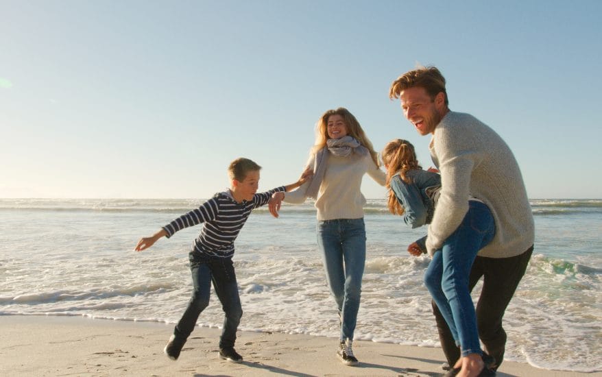 Family On Winter Beach Running Away From Advancing Waves